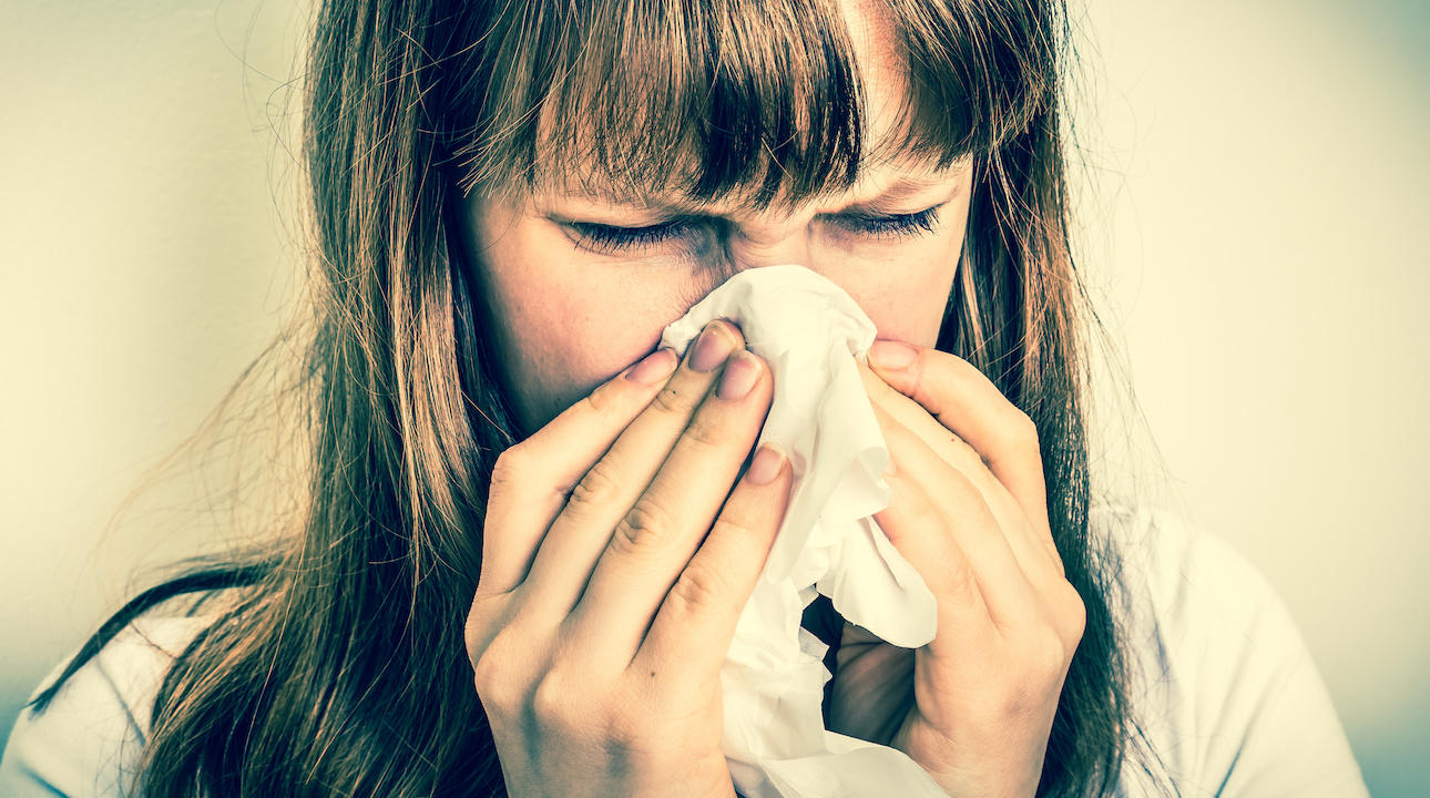 Young woman with allergy or flu cold symptoms sneezing in tissue